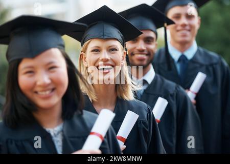 Ich bin begeistert, Absolventen zu sein. Junge Hochschulabsolventen, die ihre Diplome in der Hand halten, während sie nebeneinander stehen und lächeln. Stockfoto