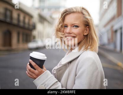 Nichts ist besser als frischer Kaffee unterwegs. Kopf- und Schulterporträt einer jungen Frau, die mit einer Tasse Kaffee auf der Straße unterwegs ist. Stockfoto