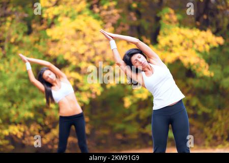 Herbstruhe. Zwei junge Frauen, die zusammen in einem Park trainieren. Stockfoto