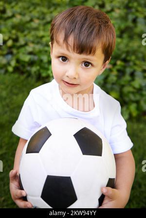 Ich will meine coolen Fußballkünste sehen. Ein süßer kleiner Junge, der draußen mit einem Fußball spielt. Stockfoto