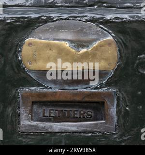 LONDON, Großbritannien - 16. NOVEMBER 2022: Schließung eines alten Briefkastens aus Messing mit abgenutztem Typenschild aus Messing an der Holztür von Lock and Co Hatters Shop in St. James's St. Stockfoto