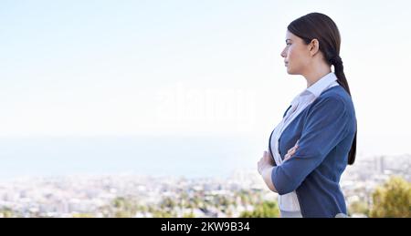 Die Aussicht genießen. Eine attraktive junge Frau, die mit der Stadt im Hintergrund steht. Stockfoto