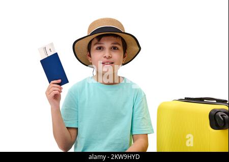 Ein bezaubernder junger Reisender mit blauem T-Shirt und Strohhut, der in den Sommerurlaub geht und die Bordkarte vor der Kamera zeigt Stockfoto