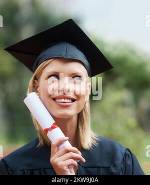 Erfolg bringt ihr ein Lächeln ins Gesicht. Ein junger College-Absolvent trägt Mütze und Kleid, während er wegsieht und lächelt. Stockfoto