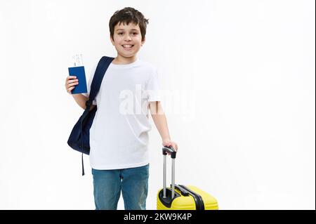 Glücklicher junger Tourist in blauen Jeans und lässigem T-Shirt mit Rucksack, Reisetasche und Bordkarte, Lächeln vor der Kamera Stockfoto