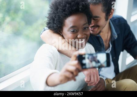 Lächeln. Eine junge Frau, die mit einem Smartphone ein Foto von sich und ihrem Freund macht. Stockfoto