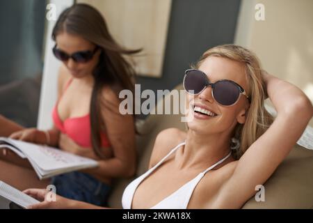 Der perfekte Tag. Zwei wunderschöne Frauen, die sich am Pool bräunen und Zeitschriften lesen. Stockfoto