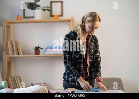Schneidekunst schneidet Kleiderstoff auf der Linie mit Nähmesser. Modedesigner Schneiderin oder Kanalisation im Werkstattstudio. Geschäftseigentümer-Shop-Konzept Stockfoto
