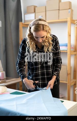 Schneiderin schneidet Kleiderstoff mit Schneiderschere. Modedesignerin im Workshop-Studio, die neue Kollektion entwirft. Geschäftsinhaber Sho Stockfoto