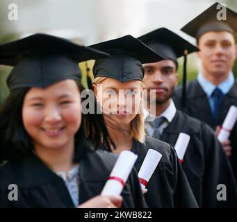 Es zahlt sich aus, zu lernen. Eine Gruppe von Hochschulabsolventen, die in Kitteln und Gewändern stehen und ihre Diplome halten. Stockfoto