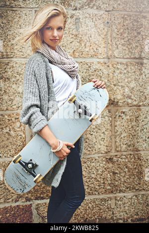 Hasst mich nicht, weil ihr mich nicht überflügeln könnt. Verkürztes Porträt einer attraktiven jungen Frau, die ihr Skateboard gegen eine Ziegelwand trug. Stockfoto