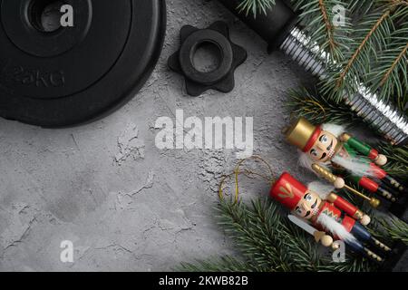 Gym-Hantelplatte, Weihnachtsnussknacker-Figuren, Baumzweige. Fitness-Feiertage, Winter-Workout flach liegend Komposition mit Kopierbereich. Stockfoto