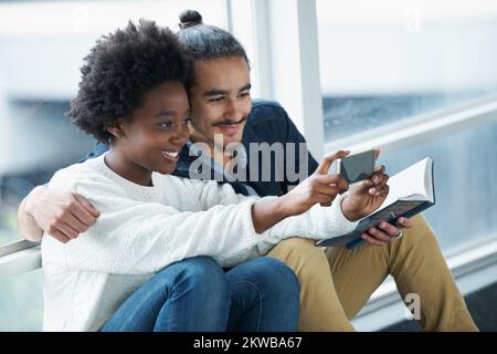 Lächeln. Ein Collegepaar, das eng zusammensitzt und Hausaufgaben macht. Stockfoto