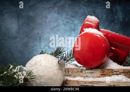 Zwei rote Kurzhanteln auf Holzscheiben, Weihnachtskugel, Äste. Komposition der Fitnessferien mit Kopierraum. Fitnesskonzept im Winter. Stockfoto