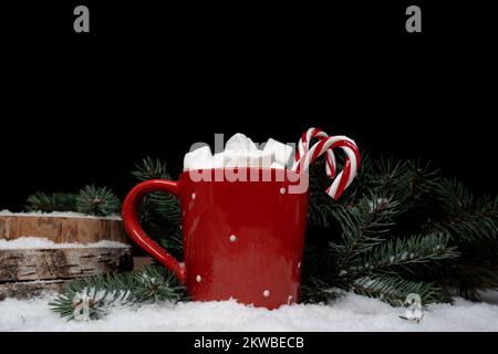 Heiße Schokolade oder Kakao mit Marshmallows und Zuckerstangen, Weihnachtsbaumzweige auf weißem Schnee. Weihnachtszeit Winterkomposition mit Kopierraum. Stockfoto