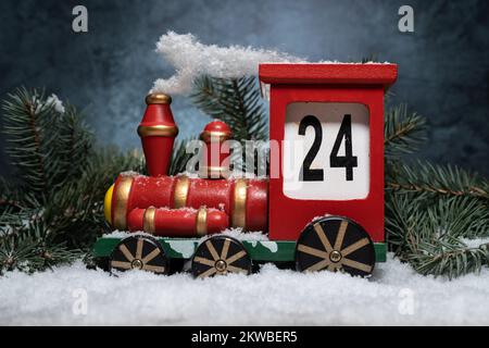 Hölzerner Zug-Adventskalender. Countdown zur Weihnachtsdekoration. Ich zähle die Tage bis Weihnachten herunter. Komposition mit Baumzweigen auf Schnee. Stockfoto