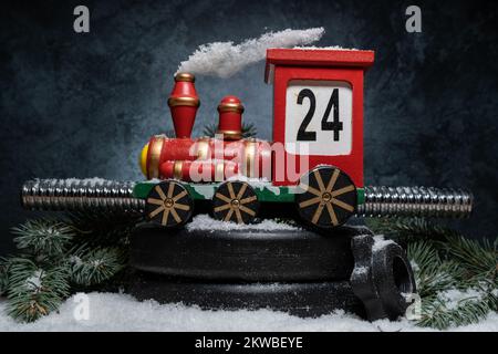 Weihnachtslieder mit Holzzug Adventskalender auf Kurzhanteln Gewichtsschildern. Dekorationsspielzeug mit Countdown. Fitness-Komposition auf Schnee. Fitnessstudio Trainingskonzept Stockfoto