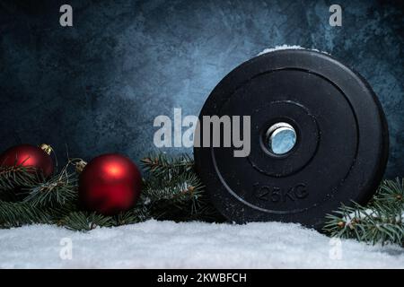 Hantelplatte, Weihnachtskugeln und Äste auf Schnee. Fitness-Feiertage Winterkomposition mit Kopierbereich. Fitnesskonzept. Stockfoto