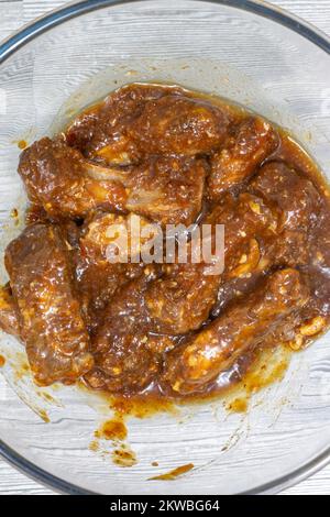 Schweinerippchen mit einer scharfen Barbecue-Sauce-Marinade in einer Glasschüssel. Auf grauem Holzhintergrund Stockfoto