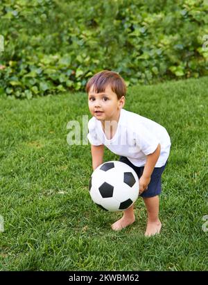 Übung ist alles. Ein süßer kleiner Junge, der draußen mit einem Fußball spielt. Stockfoto