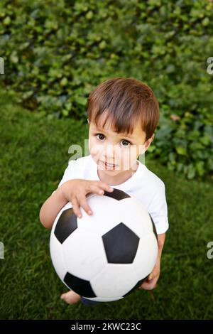 Schieß für deine Ziele. Ein süßer kleiner Junge, der draußen mit einem Fußball spielt. Stockfoto