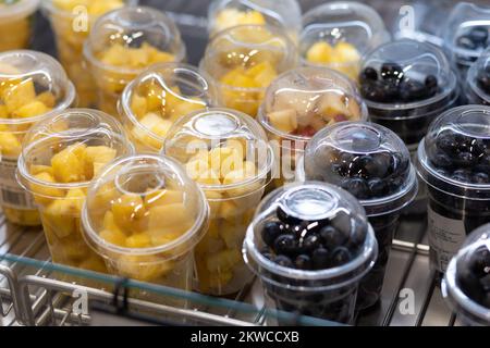 Nahaufnahme von Plastikbechern gefüllt mit gehackten Früchten und Beeren. Umweltfreundlicher, biologischer und gesunder Snack. Essen im Regal im Supermarkt. Stockfoto