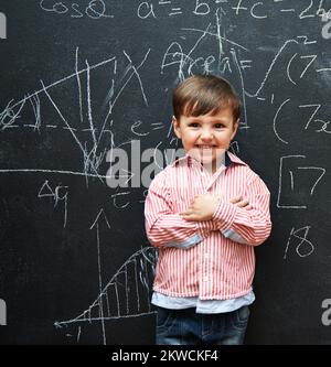 Und so wird es gemacht. Ein kleiner Junge mit einer Tafel voller mathematischer Gleichungen. Stockfoto