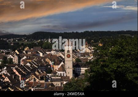 Stürmischer orangefarbener und blauer Himmel über den Giebeln, gefliesten Dächern und dem Giebelturm der gotischen Uhr der Kirche St. Johann in der Altstadt oder der Altstadt von Schaffhausen, Nordschweiz. Die verkehrsfreien Straßen sind gesäumt von vielen feinen Gotik-, Renaissance- und Barock-Gilden- oder Handelshäusern mit Orielfenstern und Fresken-Fassaden. Stockfoto