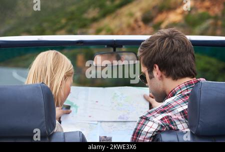 Ich denke, Sie sollten sich hier umdrehen... Rückblick auf ein junges Paar, das eine Karte liest, während es in einem Auto sitzt. Stockfoto