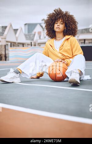 Basketball-, Platz- und Sportfrauenporträts, während Sie mit dem Ball sitzen. Stylische, trendige und Afro-Lady sieht in sportlicher Kleidung cool aus. Lässiges weibliches Model Stockfoto