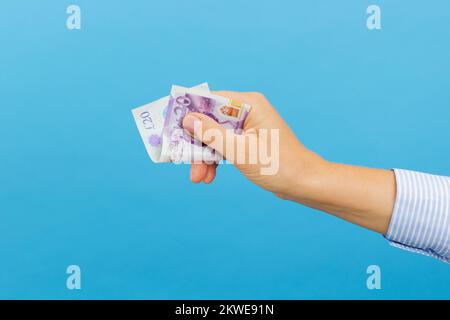 Frauenhand, die eine 20-Pfund-Banknote hält, isoliert auf blauem Hintergrund. Britische Pfund, Bargeld Stockfoto