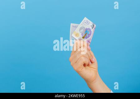 Frauenhand, die eine 20-Pfund-Banknote hält, isoliert auf blauem Hintergrund. Britische Pfund, Bargeld Stockfoto