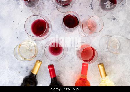 Verschiedene Weinflaschen und Weingläser mit bordeaux, Rot, Rosa und Weiß auf Betonhintergrund. Draufsicht. Abstrakte Weintapete. Stockfoto