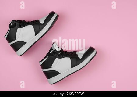 Schwarz-weiße Sneaker auf pinkfarbenem Hintergrund, Draufsicht. Stylische neue Sneaker für die Werbung in einem Schuhgeschäft Stockfoto