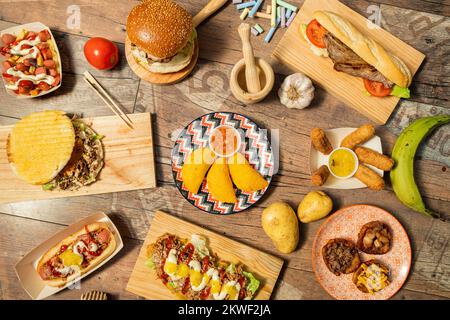 Set aus typisch lateinamerikanischen Rezepten mit kolumbianischen Maisempanadas, Salchipapas mit Sauce, Hot Dogs, tequeños mit Saucen, Patacones und Rinderbocadi Stockfoto