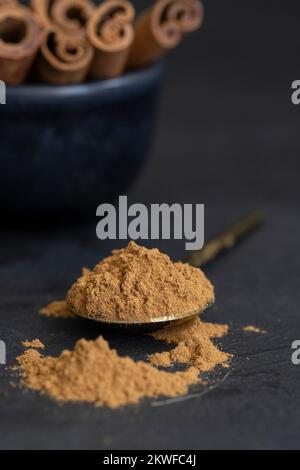 Natürliche Zimtstangen und Zimtpulver auf dunklem Betonhintergrund Stockfoto
