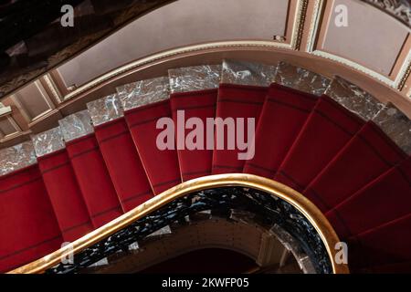 Die Wendeltreppe mit rotem Teppich geht nach unten. Klassisches Interieur, abstraktes architektonisches Hintergrundbild Stockfoto