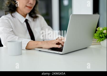 Professionelle asiatische Geschäftsfrau oder Managerin, die mit dem Laptop arbeitet, auf der Tastatur tippt oder im Büro arbeitet. Zugeschnittenes Bild und Nahaufnahme Stockfoto
