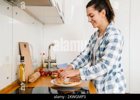 Junge Frau lächelt und macht Sandwiches in der Küche zu Hause Stockfoto