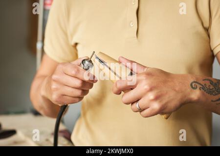 Nahaufnahme eines nicht erkennbaren tätowierten Polierrings eines Künstlers während der Herstellung von handgemachtem Schmuck mit Holzwerkzeugen, Kopierbereich Stockfoto