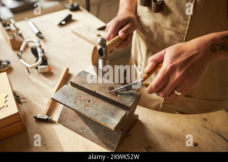 Nahaufnahme eines handgefertigten Juweliers, der einen handgefertigten Ring mit Amboss auf einer hölzernen Arbeitsstation bei Sonnenlicht und Kopierraum kreiert Stockfoto