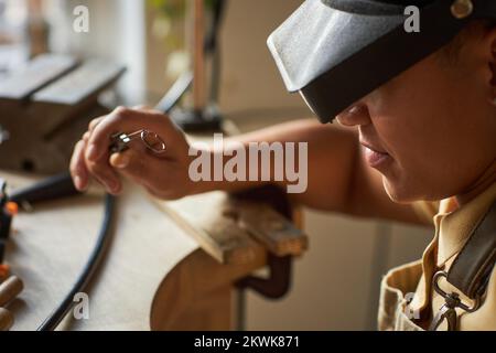 Nahaufnahme einer Juwelierin in Seitenansicht, die beim Erstellen eines Kunststücks eine Lupenbrille trägt Stockfoto