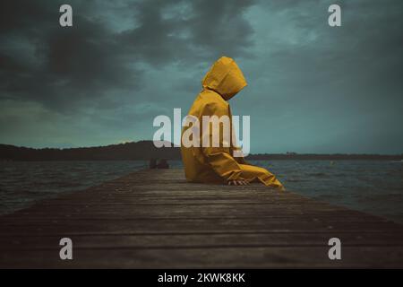 Person mit Kapuze und gelber Jacke. Dramatische Wolkenlandschaft Stockfoto