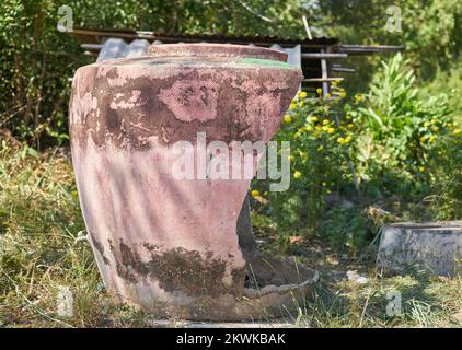 Ein großer traditioneller beschädigter Wasserbehälter auf einer Farm im ländlichen Thailand. Stockfoto