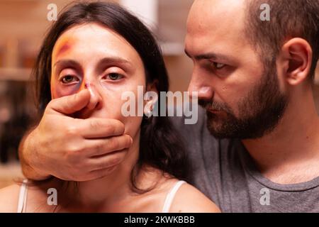Gewalttätiger Ehemann bedeckt den Mund der Frau, nachdem er ihr Gesicht geschlagen und verletzt hatte. Aggressiver Ehemann missbraucht Verletzungen erschrocken hilflos, verletzlich, Angst, geschlagen und in Panik versetzt Frau. Stockfoto