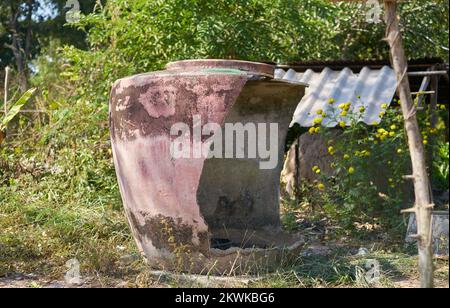 Ein großer traditioneller beschädigter Wasserbehälter auf einer Farm im ländlichen Thailand. Stockfoto