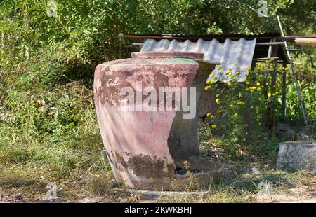 Ein großer traditioneller beschädigter Wasserbehälter auf einer Farm im ländlichen Thailand. Stockfoto