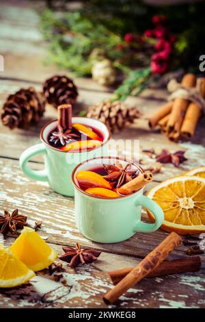 Glühwein in rustikalen Tassen mit Gewürzen und Zitrusfrüchten auf Holzhintergrund Stockfoto