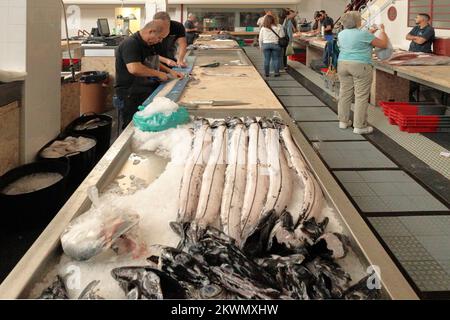 Fischmarkt Funchal, Madeira – Fischhändler, die Schwarzen Degenfisch oder Espada zubereiten, während Einkäufer den verkauften Fisch durchstöbern Stockfoto