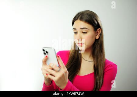 Lustige Emotionen der Freude, eine junge Frau schaut interessant auf das Telefon horizontal, den Bildschirm, sie ist sehr schönes braunes Haar Happy, junge, schöne Frau, die Spiele mit dem Handy spielt Stockfoto